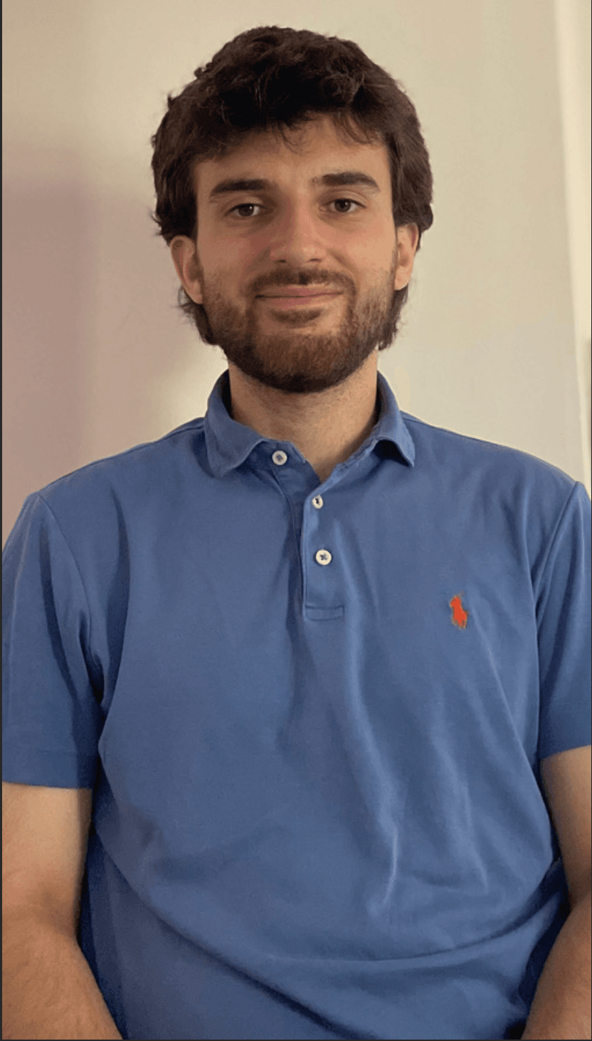 Smiling young man with dark hair and a beard wearing a blue polo shirt.